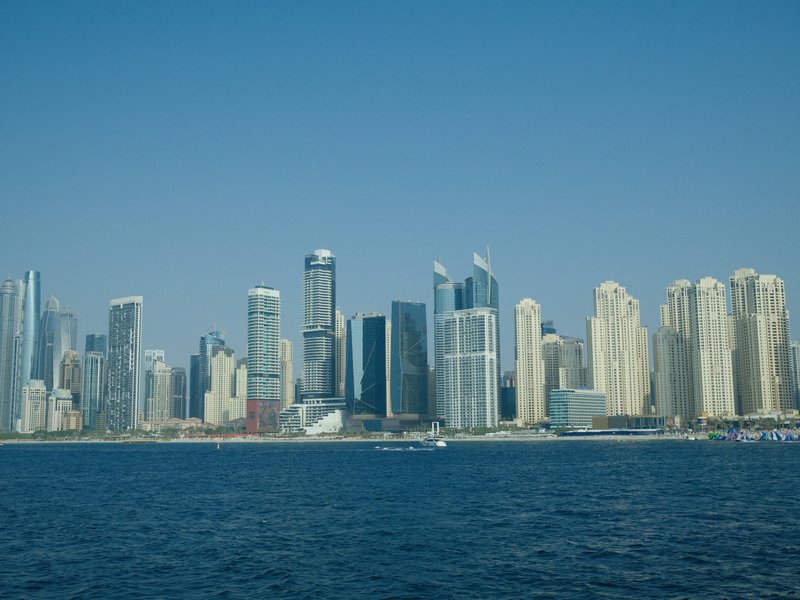 A skyline of modern skyscrapers along a waterfront under a clear blue sky.
