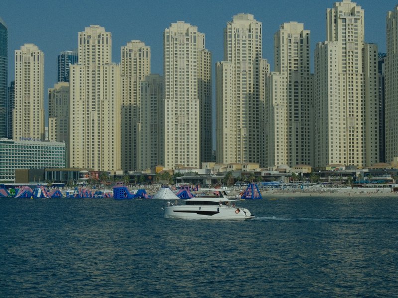 A boat cruising in front of tall skyscrapers by the water in a vibrant urban setting.