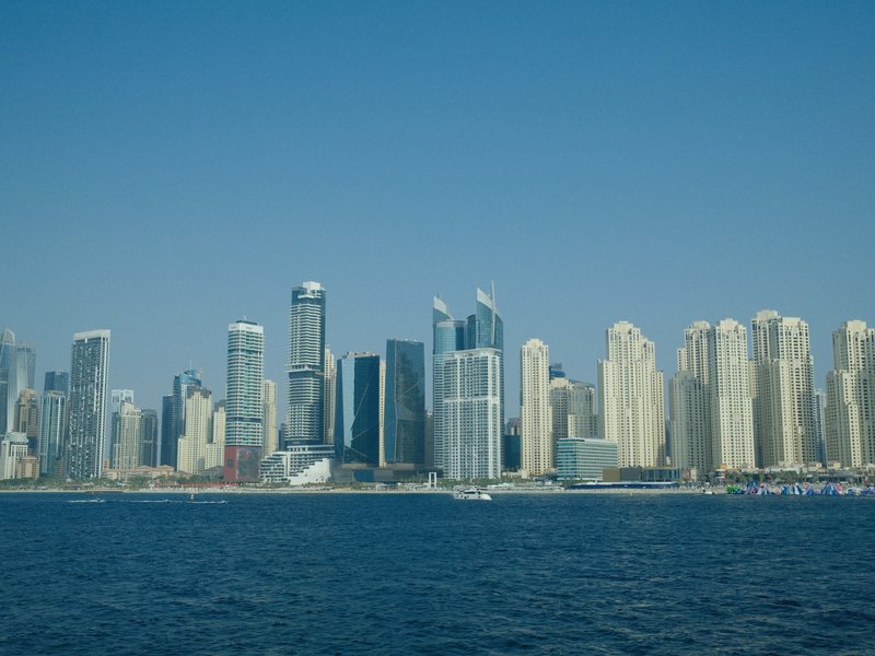 A skyline of tall buildings along a waterfront under a clear blue sky.
