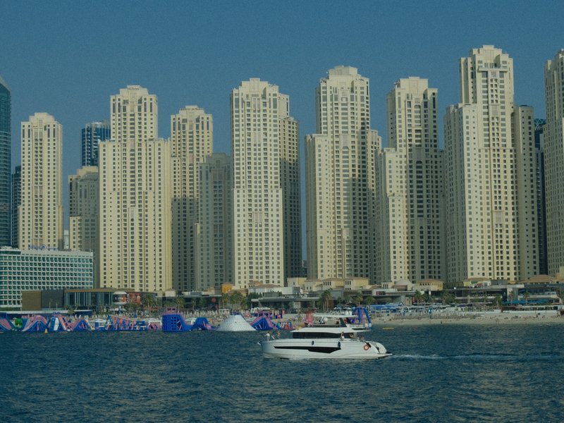 A view of tall skyscrapers along a coastline with a boat in the foreground.