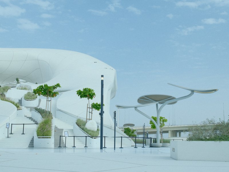 Modern architectural structure with white curves and greenery under a blue sky.