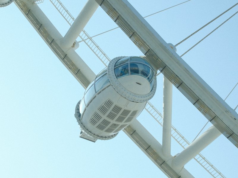 A close-up view of a white observation capsule hanging from a large white structure against a clear blue sky.