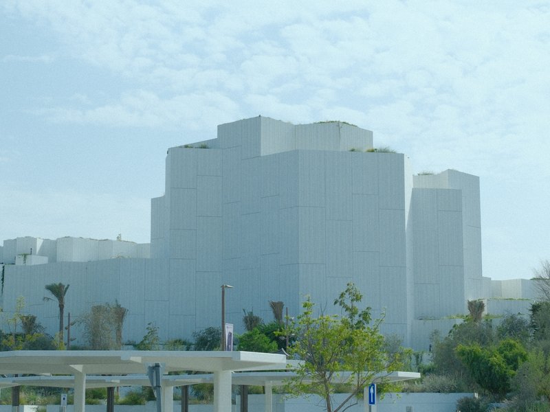 A large, modern white building with a geometric design under a cloudy sky.
