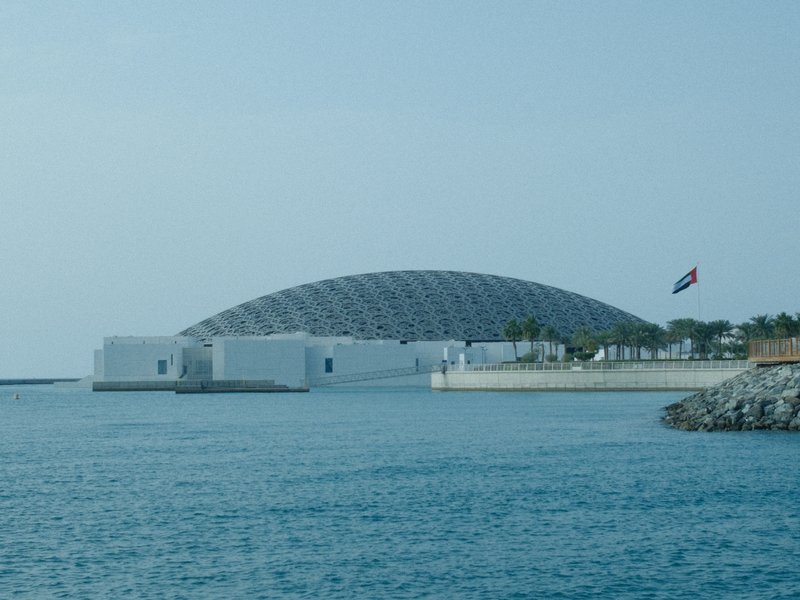 A modern architectural structure with a dome, situated by the water, under a clear sky.