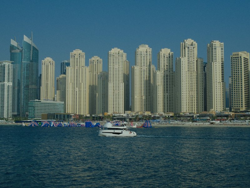 A view of tall skyscrapers along a waterfront in a city, with a boat in the foreground.