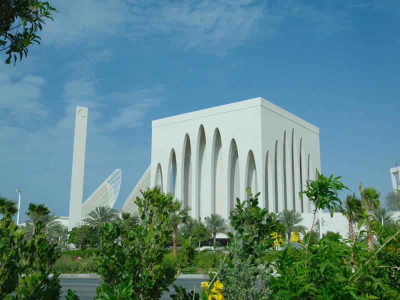 Modern architectural building with white facade surrounded by greenery under a blue sky.
