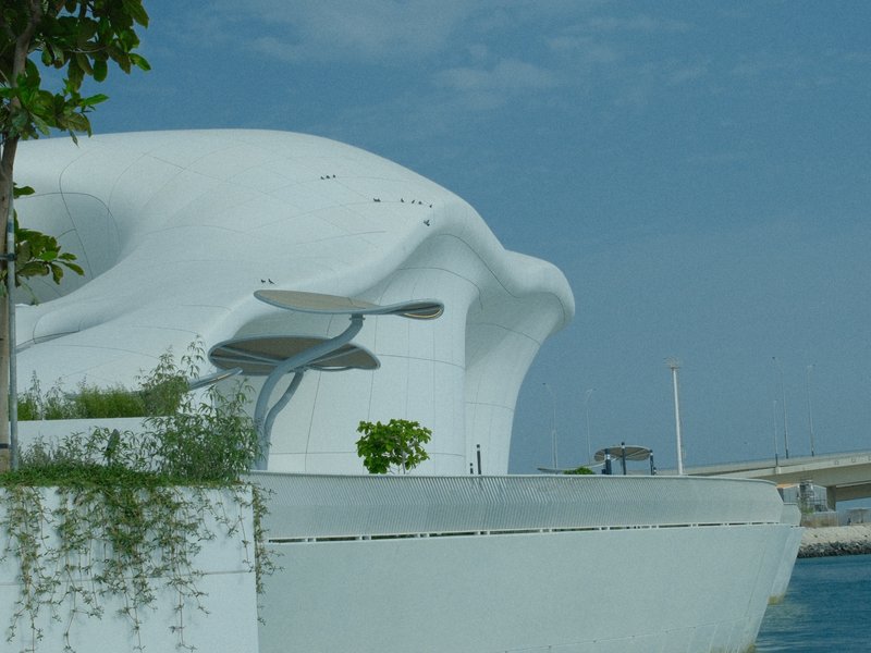 A modern white architectural structure with organic shapes near a body of water under a blue sky.