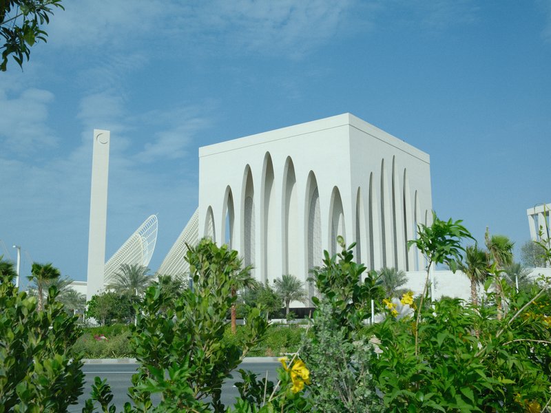 A modern white architectural building surrounded by greenery under a clear blue sky.