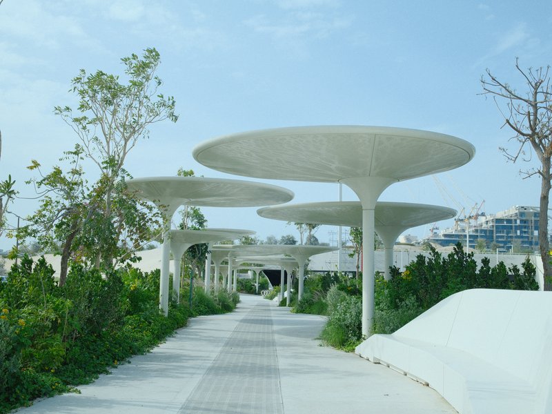 A modern pathway lined with unique mushroom-shaped structures and greenery under a clear blue sky.