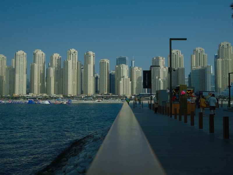 A waterfront view of tall skyscrapers lining a beach in a coastal city under a clear blue sky.