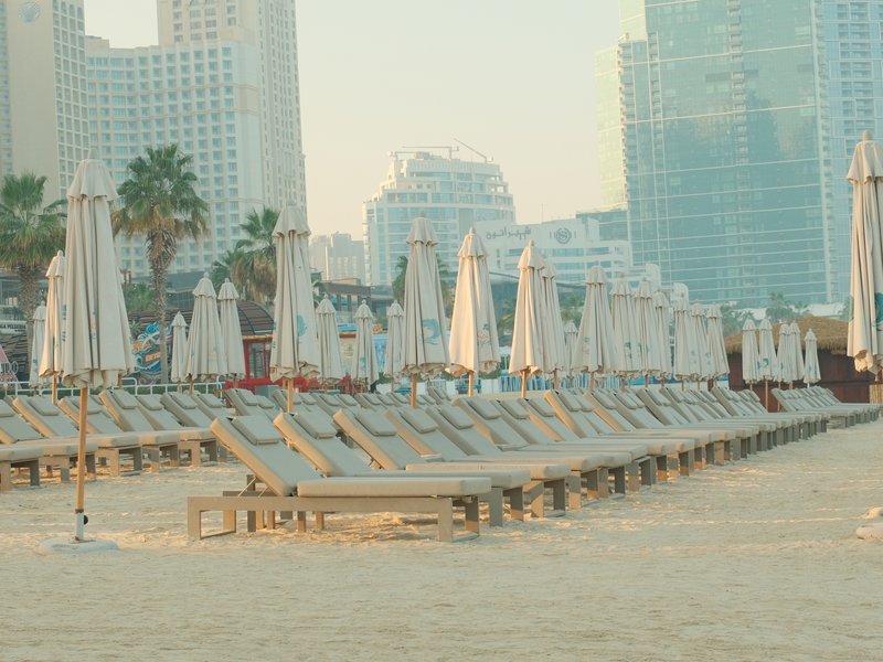 Empty beach with rows of sun loungers and umbrellas under soft morning light.