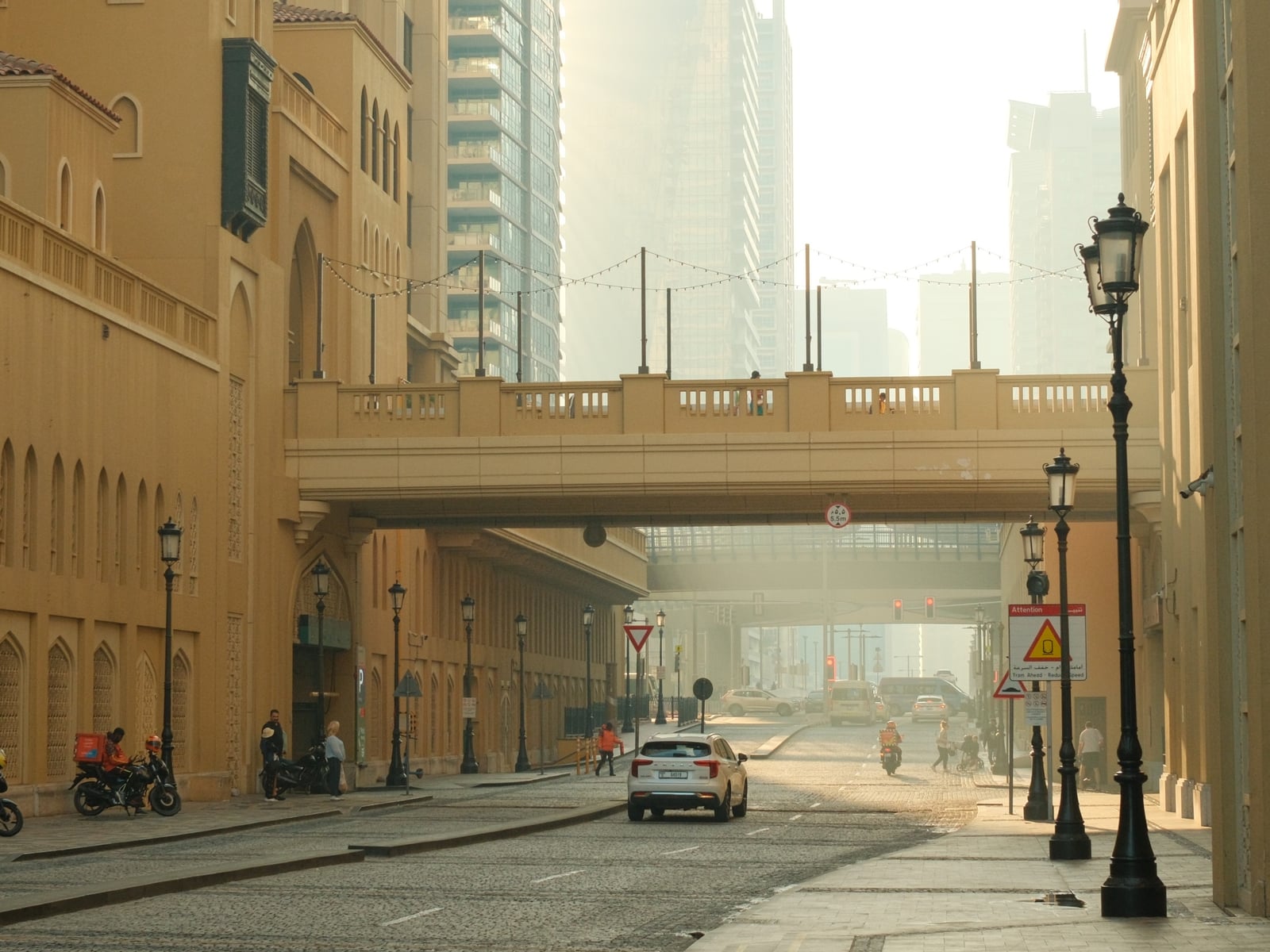 A quiet urban street with a yellow building and a bridge overhead in morning haze, shot on Portra Sol Chrome