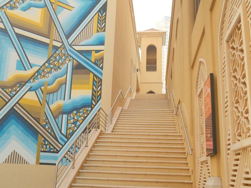 Staircase leading up with a colorful mural on the left side and a building in the background.