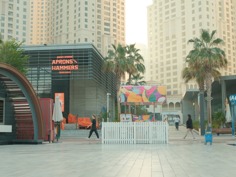 Urban scene featuring modern buildings, palm trees, and a colorful mural in a plaza.