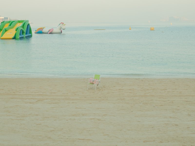 A small dog playing on a sandy beach with colorful inflatable structures in the background.