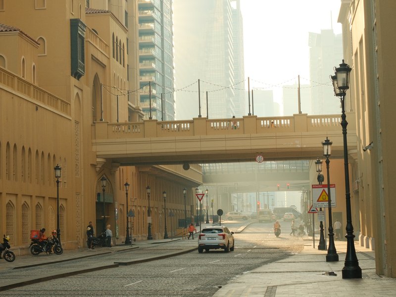 A quiet urban street with a bridge overhead, buildings in the background, and soft morning light.