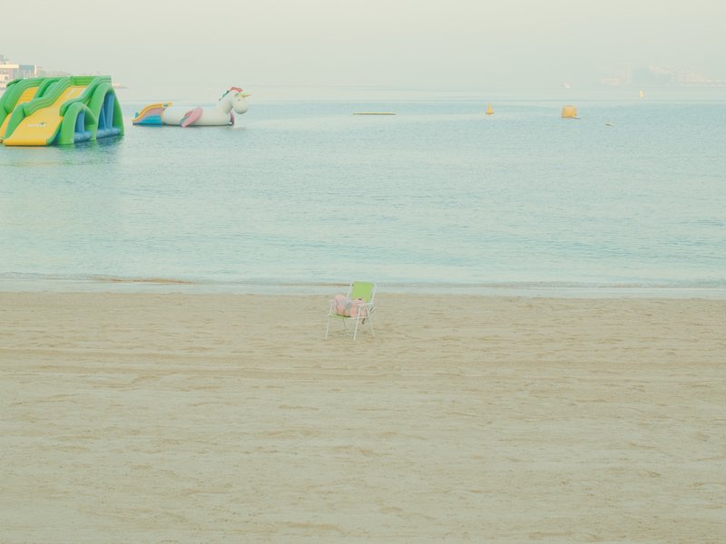 A small dog running on a sandy beach near calm water with inflatable structures in the background.