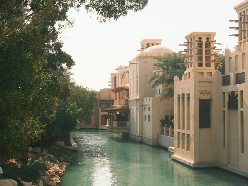 A serene canal lined with elegant buildings and lush greenery under a bright sky.