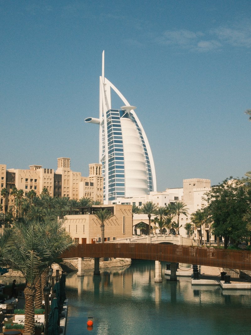 A modern skyscraper with a unique sail-like design surrounded by palm trees and a waterway.