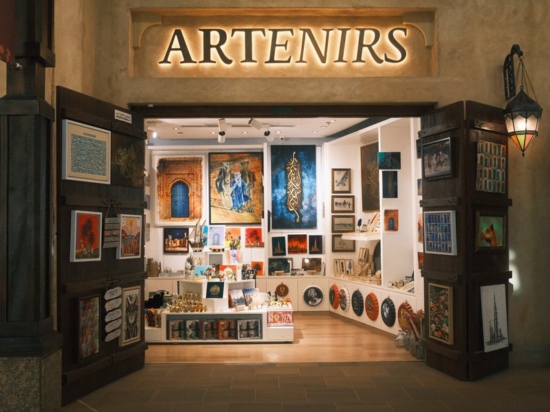 Art gallery entrance with illuminated sign and various artworks displayed inside.