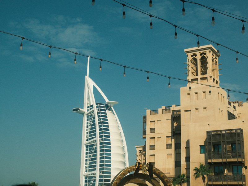 A view of the Burj Al Arab and surrounding buildings under a clear blue sky with decorative lights.