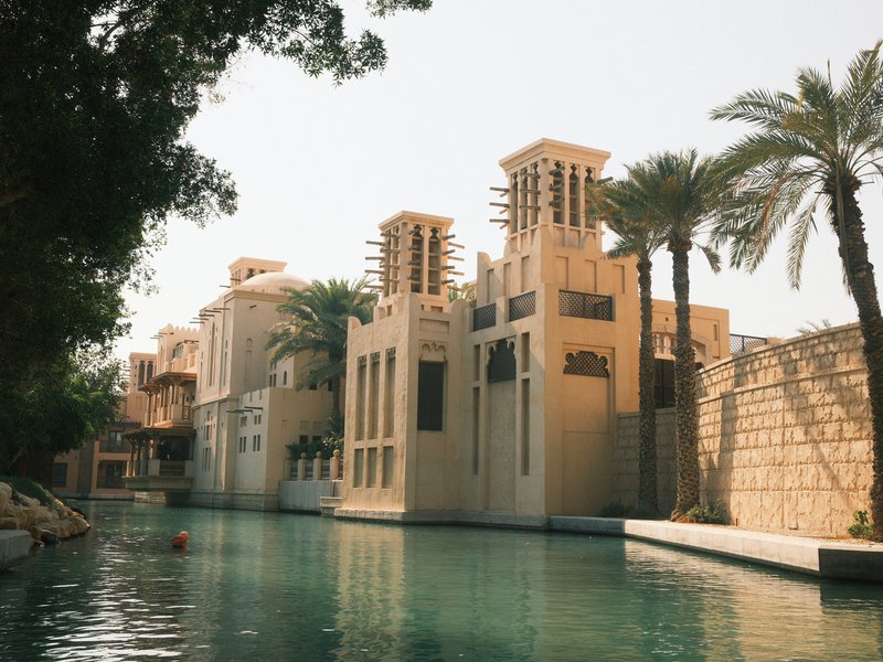 A serene canal lined with traditional Middle Eastern architecture and palm trees under a clear sky.