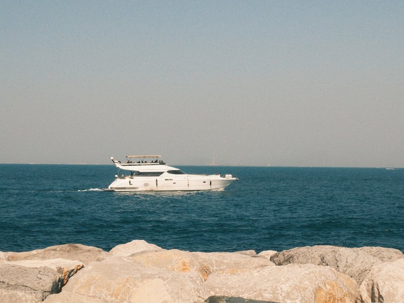 A white boat sailing on calm blue waters, with rocky shoreline in the foreground.