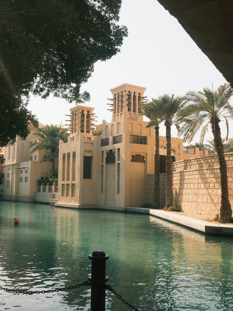 A serene view of a canal lined with palm trees and modern architecture under bright sunlight.