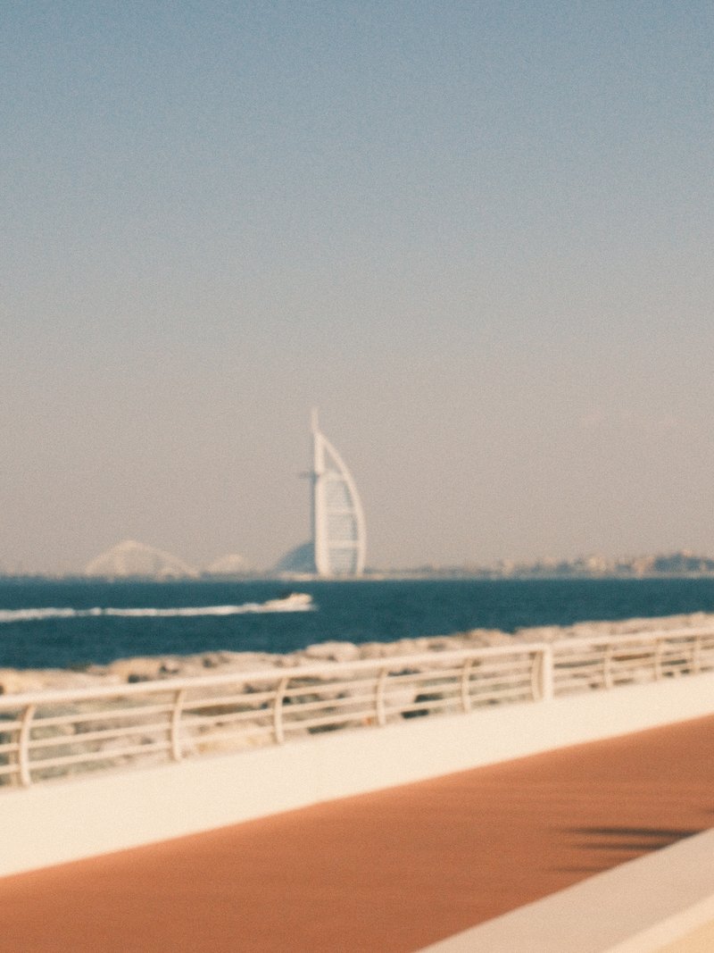 A distant view of a modern sail-shaped building by the coast, with a clear blue sky and ocean waves.