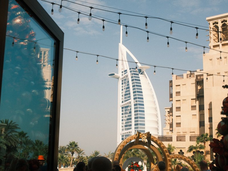 View of the Burj Al Arab hotel framed by festive decorations and string lights in an urban setting.