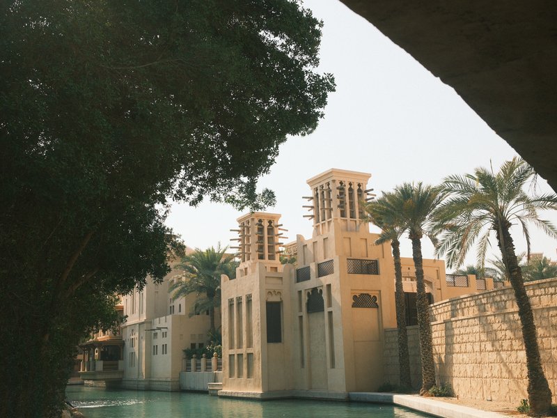 A view of a traditional building with towers beside a calm waterway, framed by palm trees.