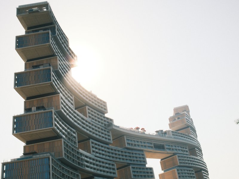 Unique architectural structure with a curved design, sun shining behind it against a clear sky.