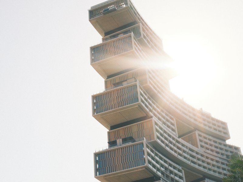 A modern architectural structure with stacked balconies, illuminated by sunlight from behind.