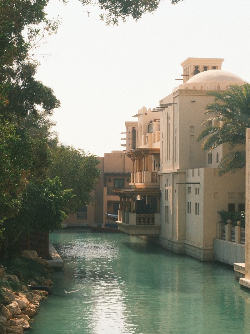 A serene canal lined with elegant buildings and palm trees under a bright sky.
