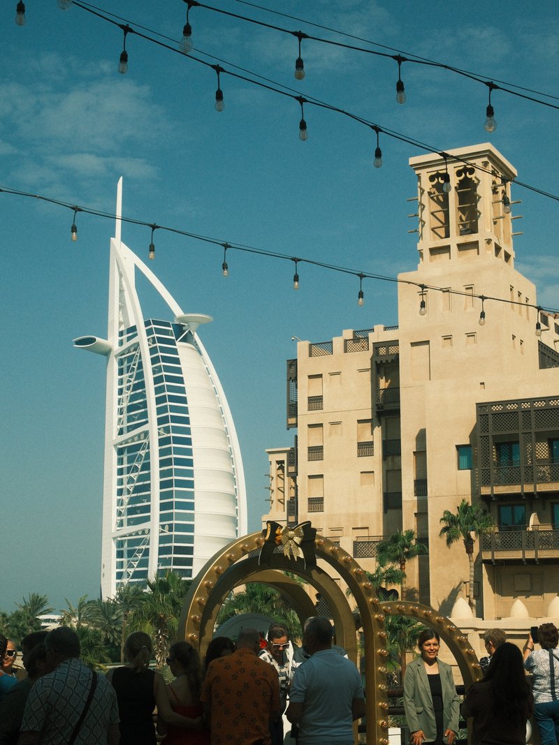 A view of the Burj Al Arab with people in the foreground and decorative lights overhead.