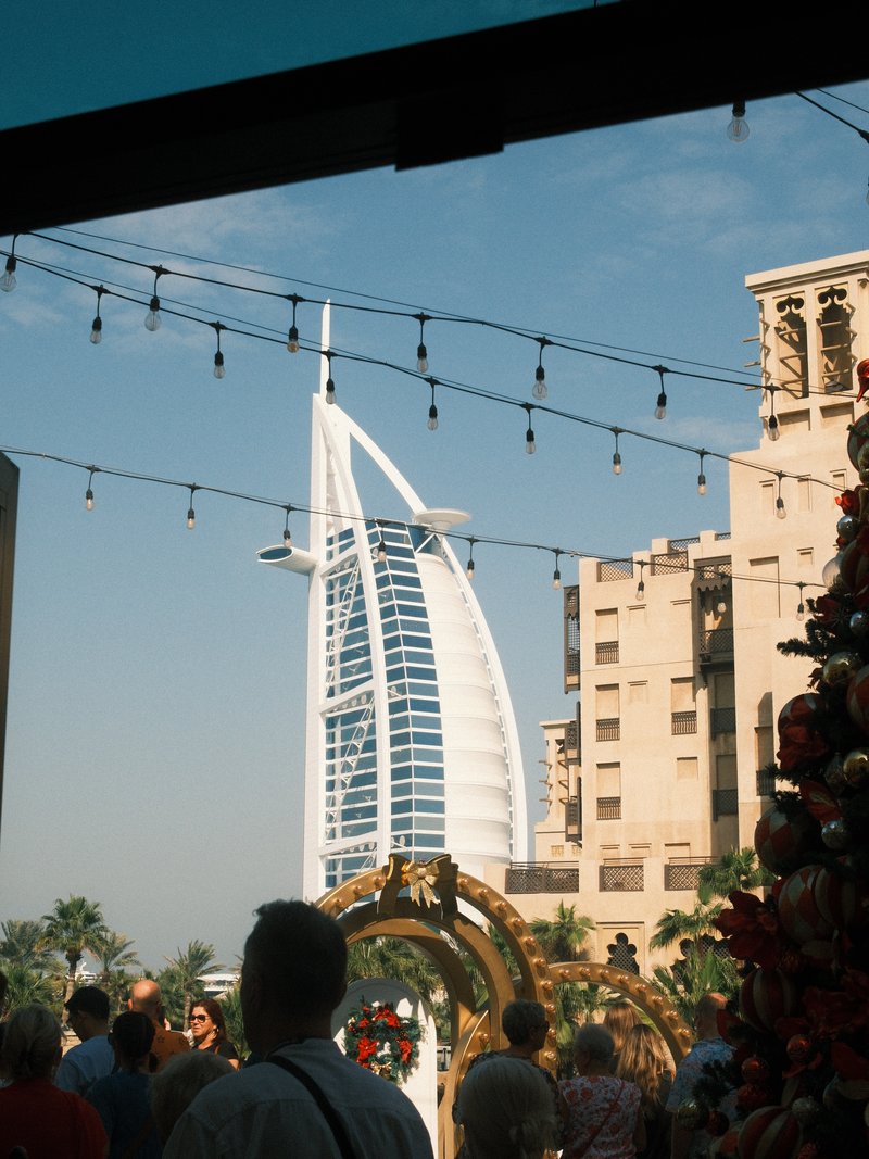 View of the Burj Al Arab hotel framed by festive decorations and people in a bustling outdoor setting.