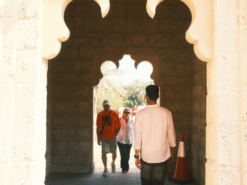 A group of people walking through an ornate archway with a stone structure in the background.