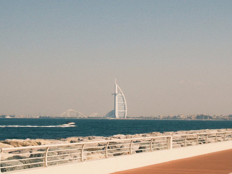 View of the Burj Al Arab hotel from a coastal promenade with a clear blue sky.