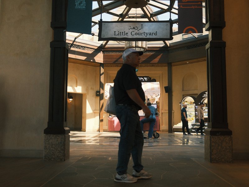 A person stands in a shopping arcade with a sign above indicating 'Little Courtyard'.