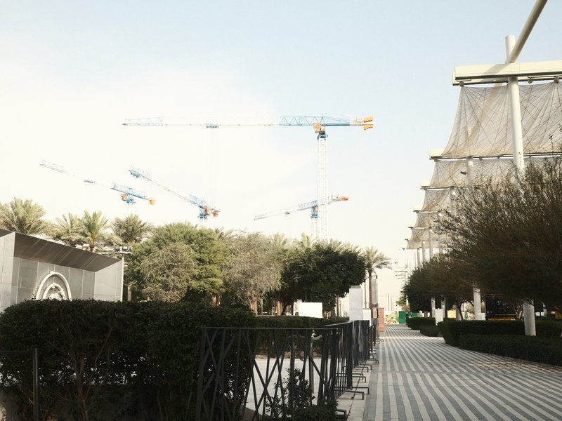 Construction site with cranes in the background, surrounded by greenery and modern architecture.