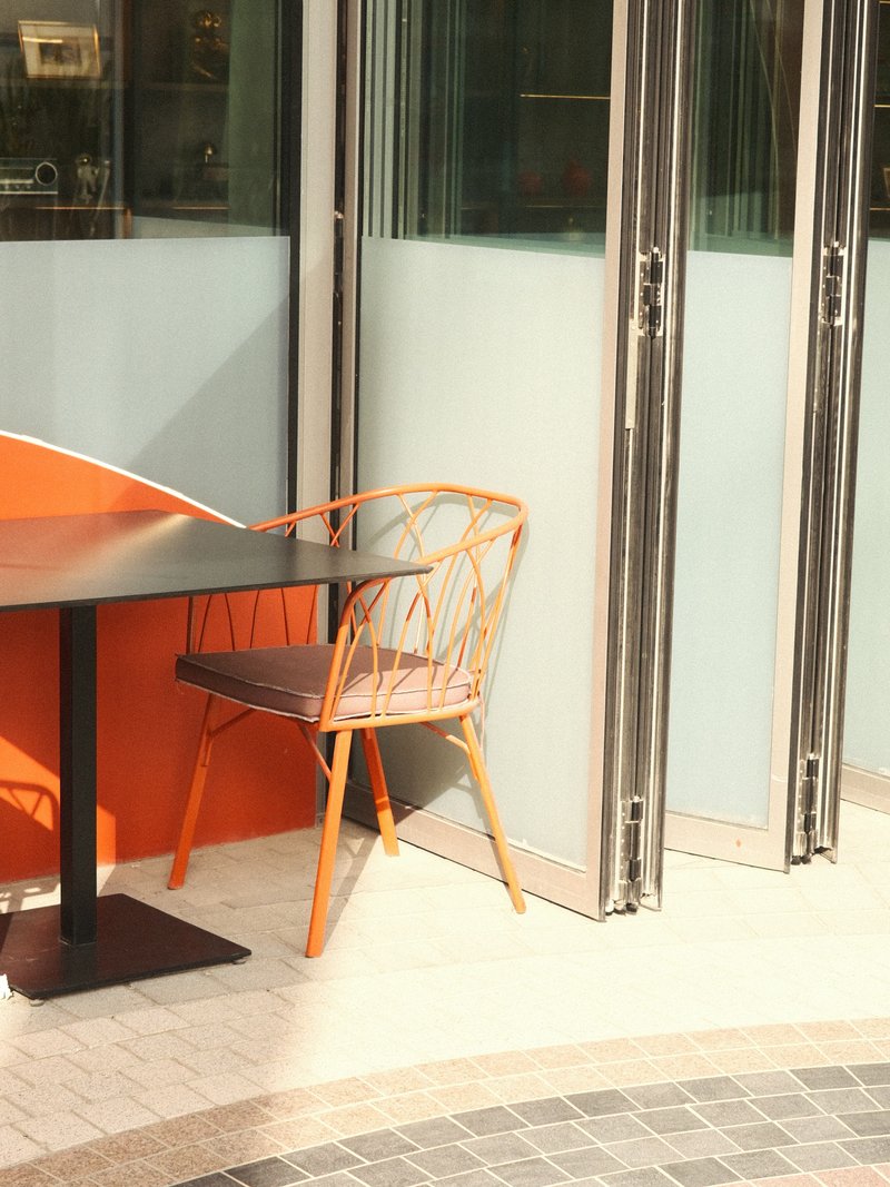 A wooden chair beside a table in a modern cafe with glass doors and orange wall accents.