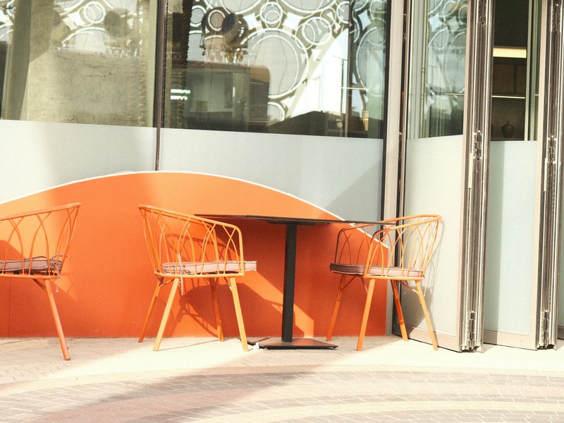 Two rattan chairs and a small table against an orange wall in a modern café setting.
