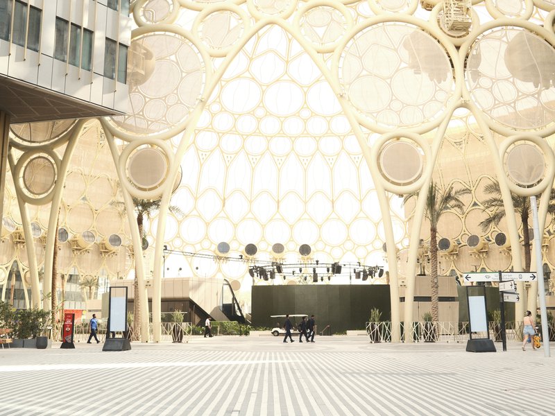A modern architectural space with intricate patterns and palm trees, featuring people walking.