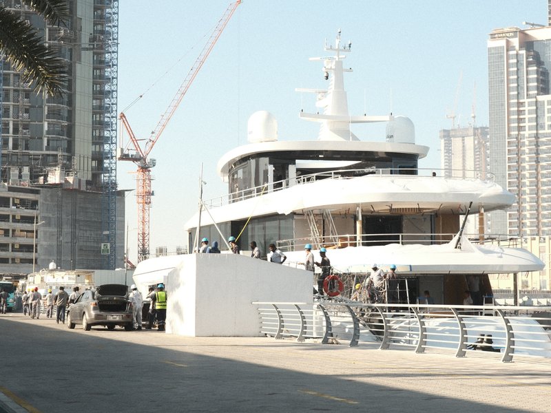 A large yacht docked at a marina with construction cranes and buildings in the background.
