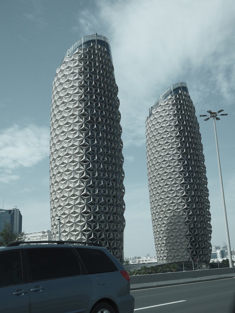 Two modern skyscrapers with unique architectural designs against a cloudy sky.
