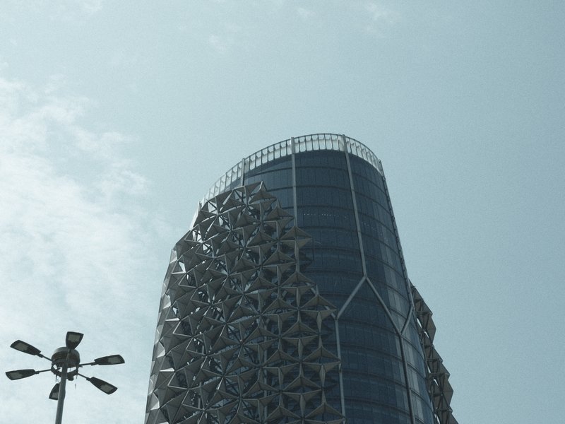 A modern building with intricate patterns on its facade against a pale blue sky.