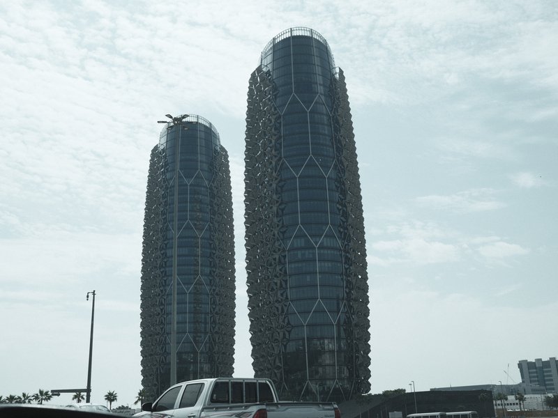 Two modern skyscrapers with unique architectural designs under a cloudy sky.