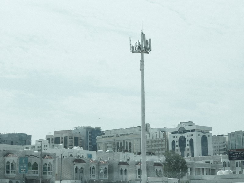 A cityscape featuring a cell tower amidst modern buildings under a cloudy sky.