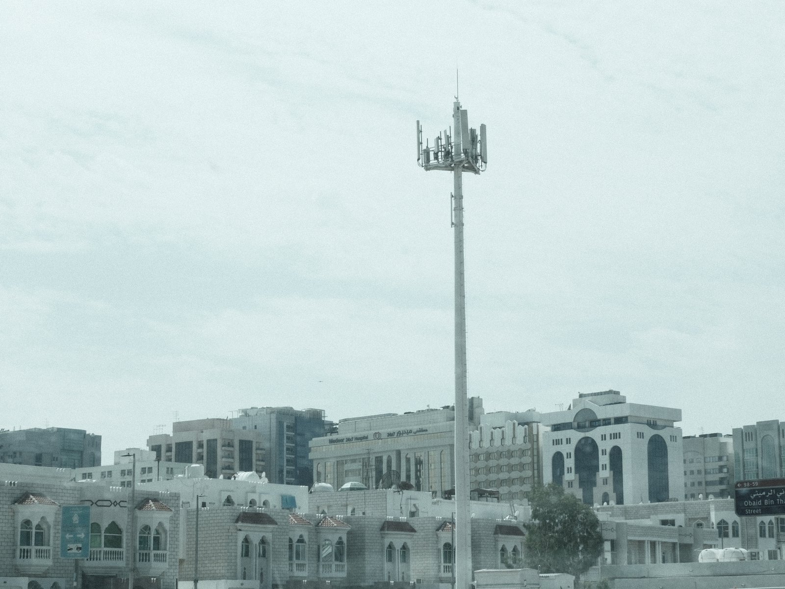 A cityscape featuring a cell tower amidst modern buildings under a cloudy sky.