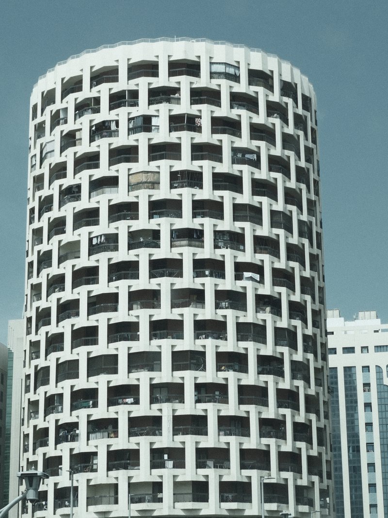 A cylindrical building with a unique lattice-like facade against a clear blue sky.